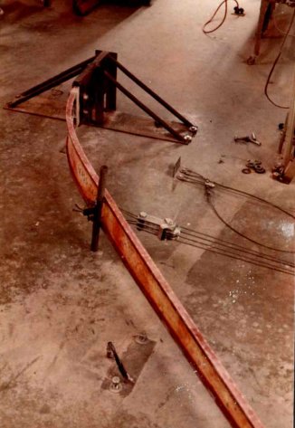 A blade root section under a load rig on the workshop floor, set up to bend the filament-wound spar at its attachment to the root fitting