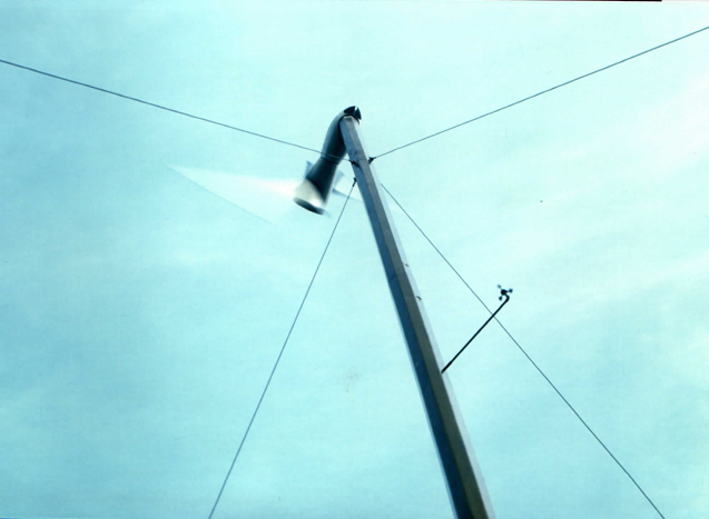 Looking up the guyed tower with the rotor running — the downwind machine yaws freely on its slender monopole.