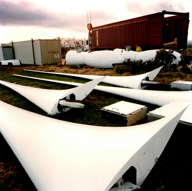 Rotor blades and nacelle bodies in the laydown area — the complete turbine ships in standard ISO containers and is staged on site.